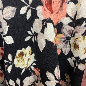 May include: Black fabric with a floral pattern featuring pink, white, and green roses. The fabric has a textured surface.