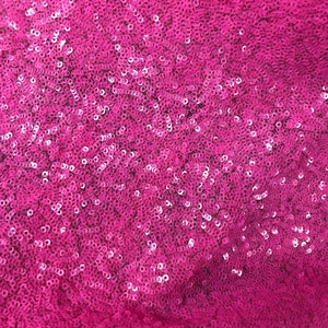 May include: Close-up of a pink fabric covered in sequins. The sequins are small and round, and they create a shimmering effect.