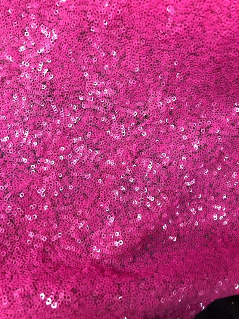 May include: Close-up of a pink fabric covered in sequins. The sequins are small and round, and they create a shimmering effect.