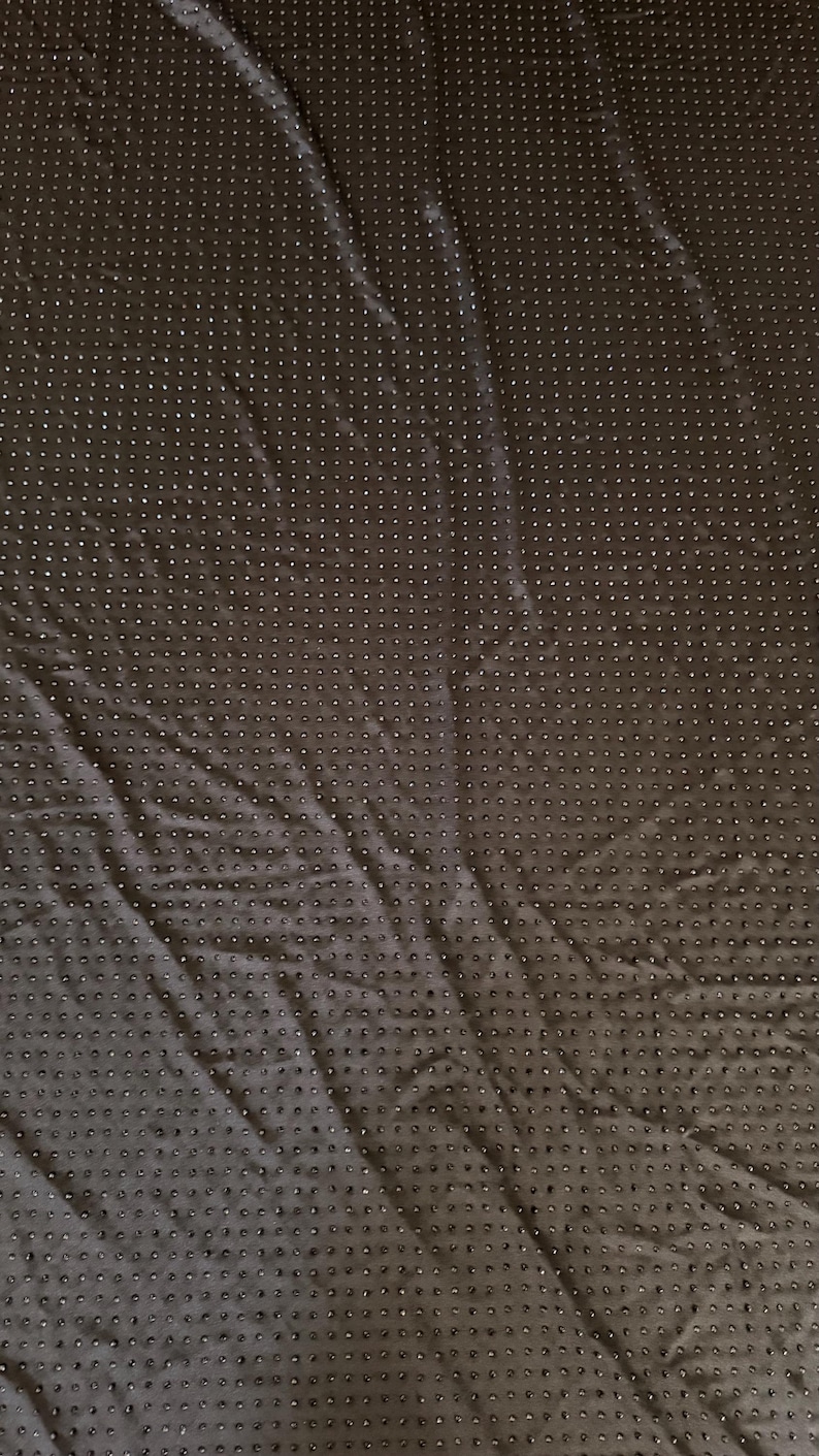 Op de afbeelding: Een donkerbruine stof met een uniform raster van kleine, verhoogde, cirkelvormige siliconen stippen over het gehele oppervlak. Het textiel heeft een licht gekreukelde textuur en een matte afwerking, ontworpen met een functioneel antislippatroon.