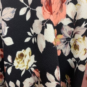 May include: Black fabric with a floral pattern featuring pink, white, and brown roses. The fabric has a textured surface.