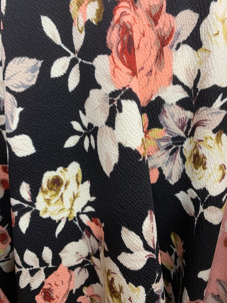 May include: Black fabric with a floral pattern featuring pink, white, and brown roses. The fabric has a textured surface.