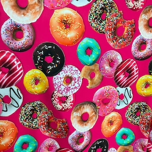 Può includere: Uno sfondo rosa con un motivo ripetuto di ciambelle colorate con diverse guarnizioni. Le ciambelle sono di forme e dimensioni diverse, tra cui glassate, con codette, al cioccolato e ripiene di gelatina.