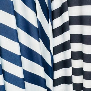 K&ouml;nnte beinhalten: Nahaufnahme von drei Stoffen mit kr&auml;ftigen, diagonalen Streifen. Die Stoffe weisen marineblaue und wei&szlig;e Streifen sowie schwarz-wei&szlig;e Streifen auf. Der Stoff ist drapiert und erzeugt weiche Falten und Schatten.