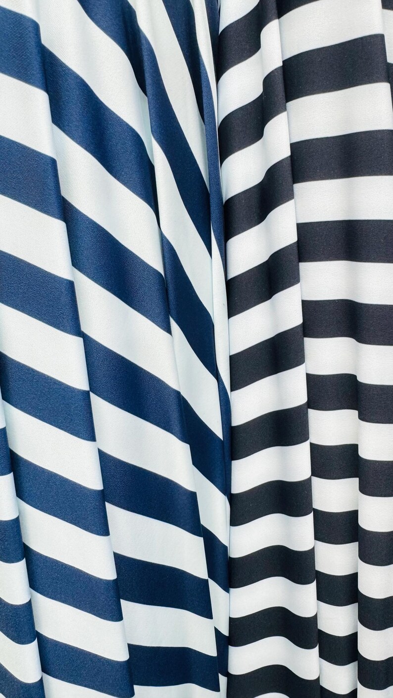 K&ouml;nnte beinhalten: Nahaufnahme von drei Stoffen mit kr&auml;ftigen, diagonalen Streifen. Die Stoffe weisen marineblaue und wei&szlig;e Streifen sowie schwarz-wei&szlig;e Streifen auf. Der Stoff ist drapiert und erzeugt weiche Falten und Schatten.