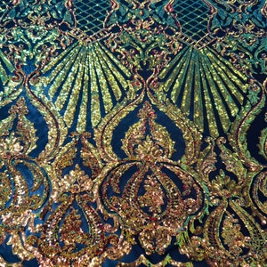 May include: A close-up of a dark blue fabric with a gold and red sequined pattern. The pattern features a repeating design of ornate swirls and arches.