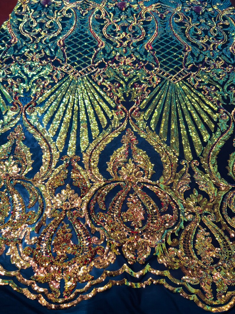 May include: A close-up of a dark blue fabric with a gold and red sequined pattern. The pattern features a repeating design of ornate swirls and arches.