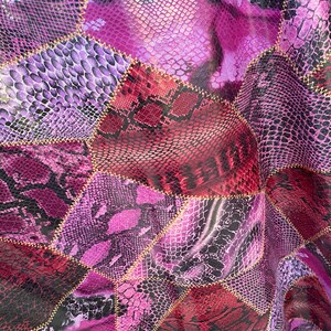 May include: A fabric with a patchwork design featuring various shades of purple and red. The fabric has a snakeskin pattern and is stitched together with gold thread.