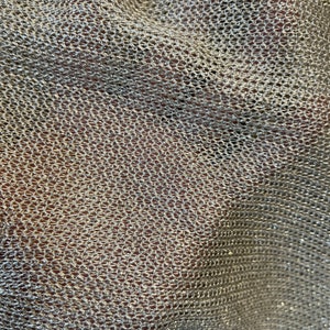 Puede incluir: Primer plano de una tela met&aacute;lica plateada con una textura tejida en forma de malla. La tela tiene un brillo sutil y est&aacute; ligeramente arrugada.