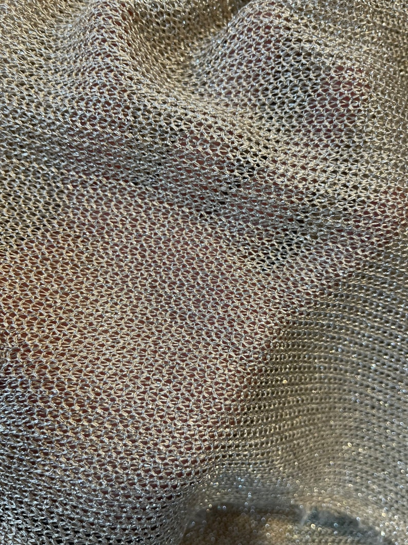 Puede incluir: Primer plano de una tela met&aacute;lica plateada con una textura tejida en forma de malla. La tela tiene un brillo sutil y est&aacute; ligeramente arrugada.