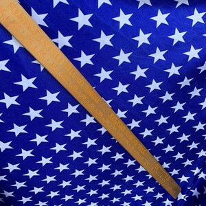 May include: Blue fabric with a white star pattern. A wooden ruler with inch markings is placed diagonally across the fabric.