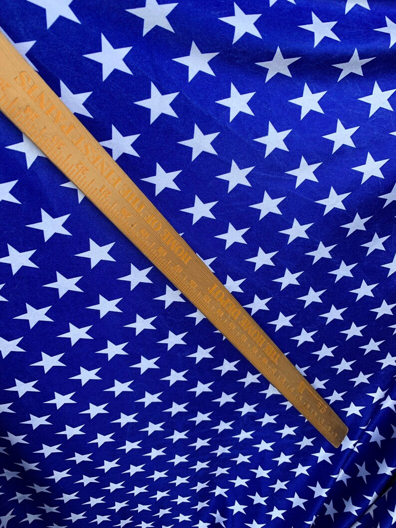 May include: Blue fabric with a white star pattern. A wooden ruler with inch markings is placed diagonally across the fabric.