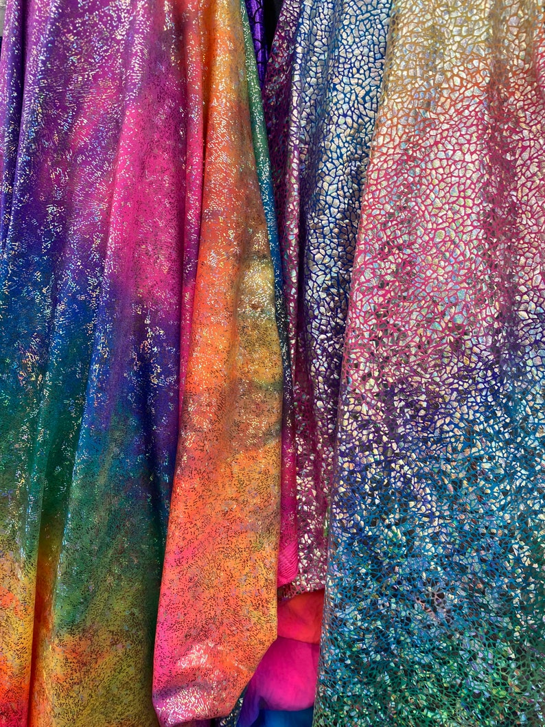 K&ouml;nnte beinhalten: Vier schimmernde Stoffmuster mit einem Regenbogen-Verlaufsmuster. Der Stoff hat eine strukturierte, glitzernde Oberfl&auml;che.