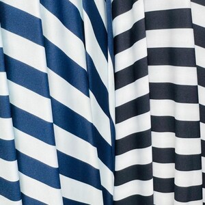 K&ouml;nnte beinhalten: Nahaufnahme von zwei Stoffen mit kr&auml;ftigen, diagonalen Streifen. Ein Stoff hat marineblaue und wei&szlig;e Streifen, der andere schwarz-wei&szlig;e Streifen. Die Stoffe sind drapiert und erzeugen weiche Falten und Schatten.