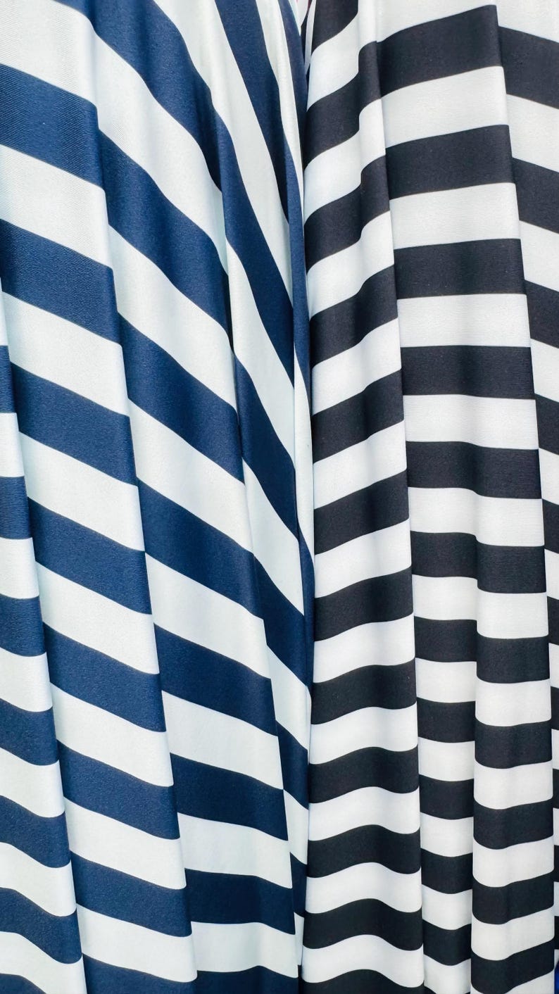 K&ouml;nnte beinhalten: Nahaufnahme von zwei Stoffen mit kr&auml;ftigen, diagonalen Streifen. Ein Stoff hat marineblaue und wei&szlig;e Streifen, der andere schwarz-wei&szlig;e Streifen. Die Stoffe sind drapiert und erzeugen weiche Falten und Schatten.