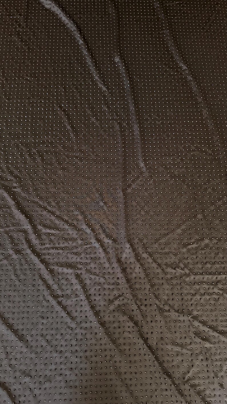 Op de afbeelding: Een donkerbruin stoffen oppervlak met een uniform raster van kleine, verhoogde, ronde siliconen stippen. Het materiaal oogt flexibel en licht gekreukt, waarbij de textuur van de stippen een consistent patroon vormt over het gehele zichtbare gebied.