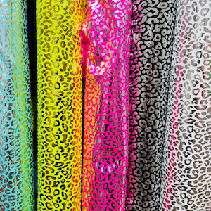 Może przedstawiać: Pionowa prezentacja rolek materiału z nadrukiem w cętki. Rolki prezentują różnorodne kolory, w tym turkusowy, żółty, różowy, czarny i biały. Cętki mają metaliczny połysk, dodając tkaninie odrobinę blasku.