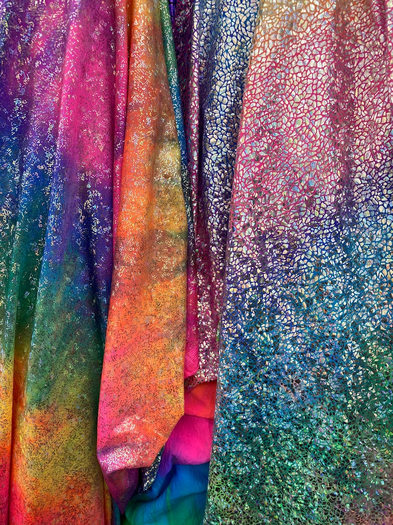 K&ouml;nnte beinhalten: Vier verschiedene irisierende Stoffe mit einem Regenbogenfarbverlauf. Die Stoffe haben eine strukturierte, glitzernde Oberfl&auml;che.