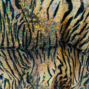 May include: Close-up of a brown and black tiger print fabric with iridescent glitter accents. The fabric has a textured, almost furry look.