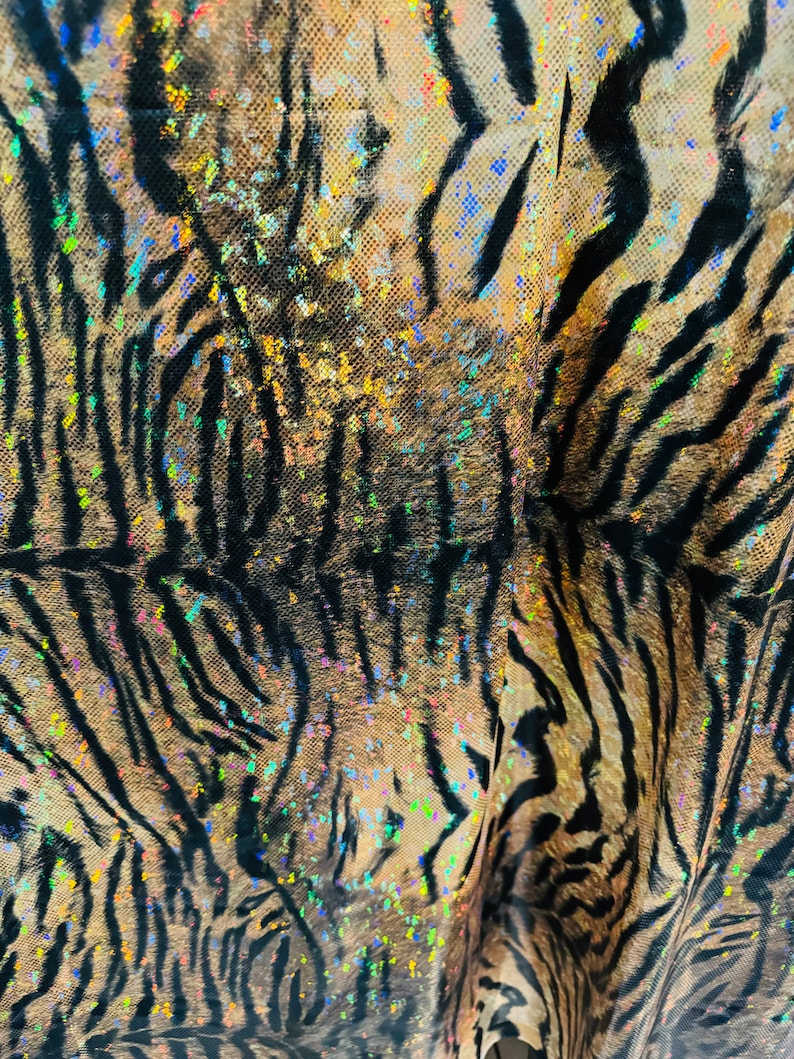May include: Close-up of a brown and black tiger print fabric with iridescent glitter accents. The fabric has a textured, almost furry look.