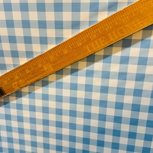 K&ouml;nnte beinhalten: Ein Nahaufnahme von blau-wei&szlig;em Gingham-Stoff mit einem Holzlineal darauf. Das Lineal ist in Zoll eingeteilt.