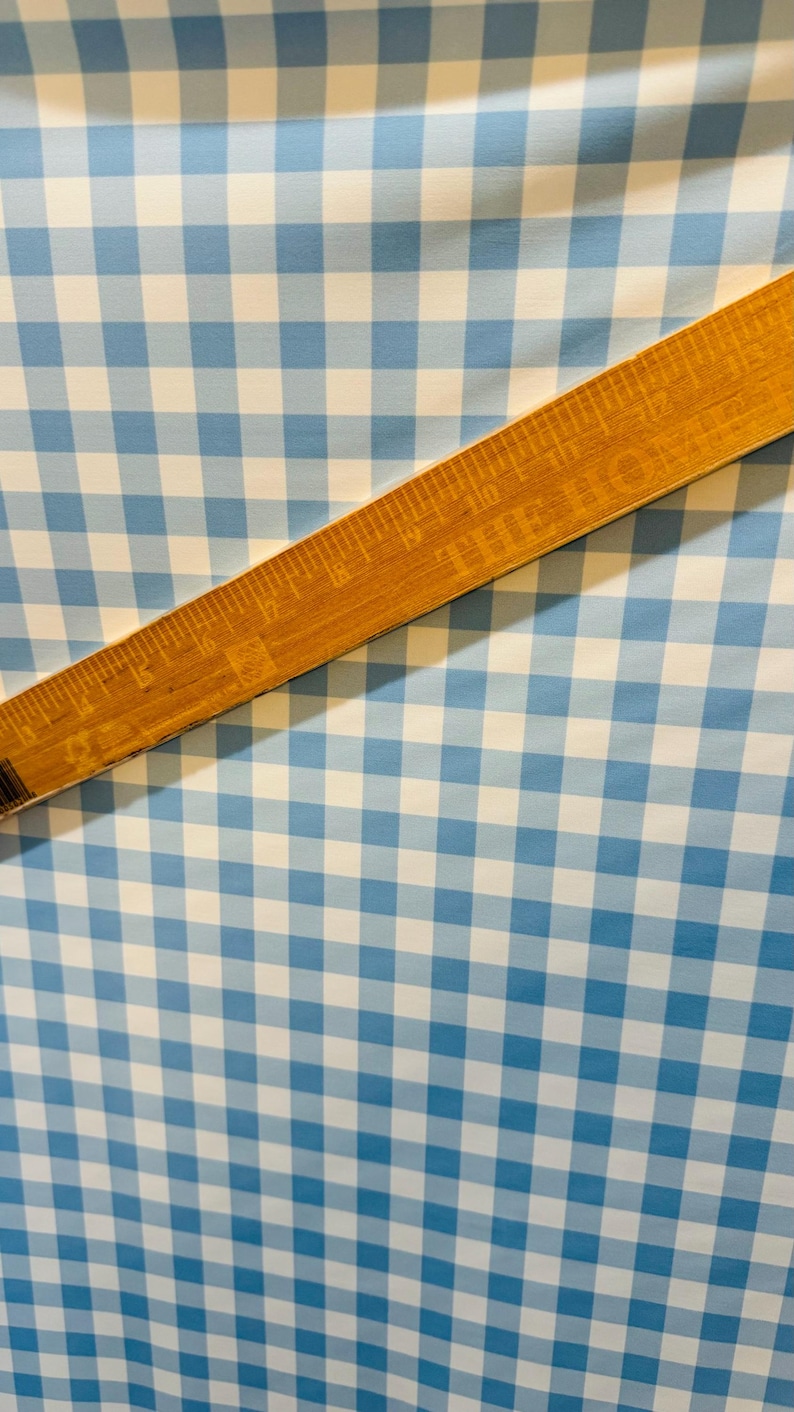 K&ouml;nnte beinhalten: Ein Nahaufnahme von blau-wei&szlig;em Gingham-Stoff mit einem Holzlineal darauf. Das Lineal ist in Zoll eingeteilt.