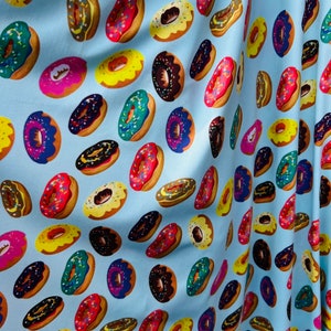 May include: A blue fabric with a repeating pattern of colourful doughnuts. The doughnuts have different toppings, including sprinkles, chocolate, and frosting.