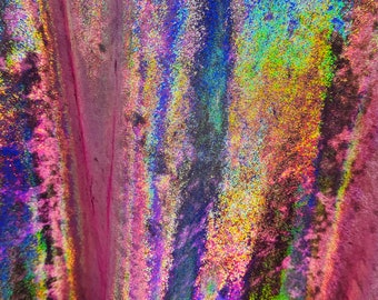 May include: Close-up of iridescent fabric with a textured, velvet-like surface. The fabric has a multi-colored, holographic sheen with shades of pink, blue, green, and yellow.