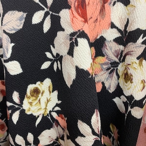 May include: Black fabric with a floral pattern featuring pink, white, and brown roses. The fabric has a textured surface.