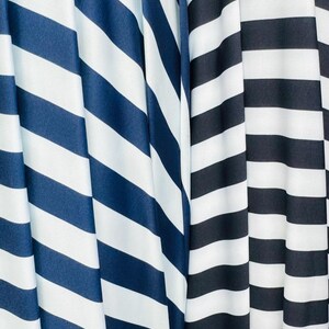 K&ouml;nnte beinhalten: Nahaufnahme von zwei Stoffen mit kr&auml;ftigen, diagonalen Streifen. Ein Stoff hat marineblaue und wei&szlig;e Streifen, w&auml;hrend der andere schwarz-wei&szlig;e Streifen aufweist. Die Stoffe sind drapiert und erzeugen weiche Falten und Schatten.