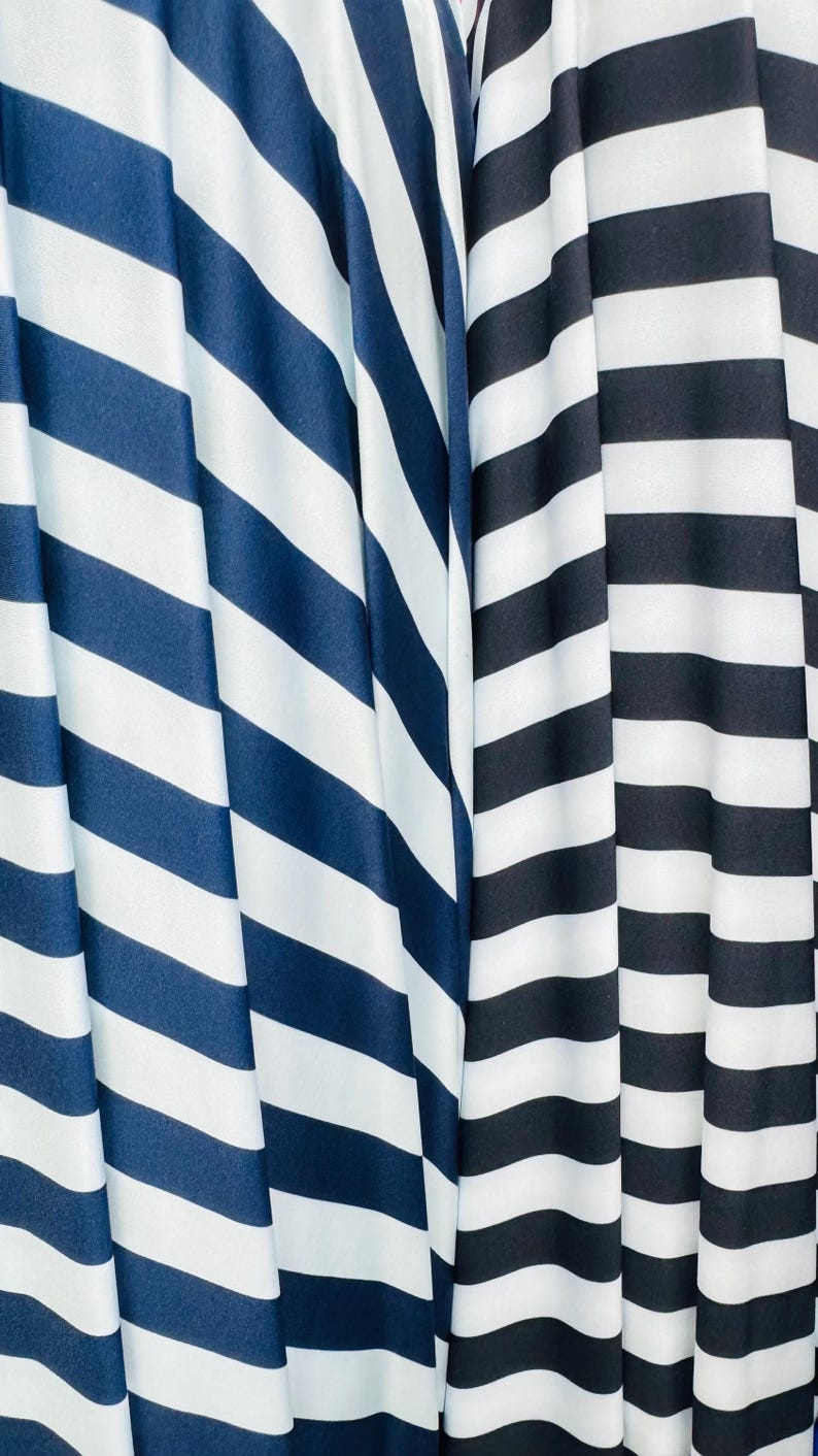 K&ouml;nnte beinhalten: Nahaufnahme von zwei Stoffen mit kr&auml;ftigen, diagonalen Streifen. Ein Stoff hat marineblaue und wei&szlig;e Streifen, w&auml;hrend der andere schwarz-wei&szlig;e Streifen aufweist. Die Stoffe sind drapiert und erzeugen weiche Falten und Schatten.