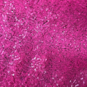 May include: A close-up of a fabric covered in pink sequins. The sequins are small and tightly packed together, creating a shimmering effect.