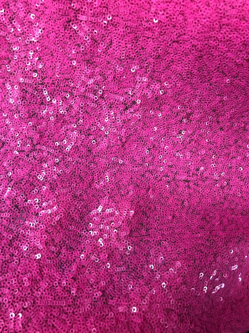 May include: A close-up of a fabric covered in pink sequins. The sequins are small and tightly packed together, creating a shimmering effect.