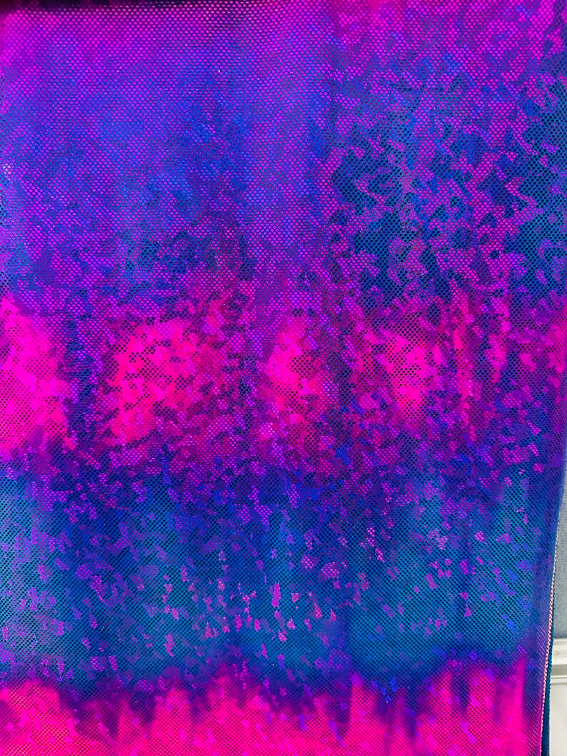 Op de afbeelding: Een close-up van een iriserende stof met een blauw en roze ombre-patroon. De stof heeft een textuur en een glinsterende afwerking.