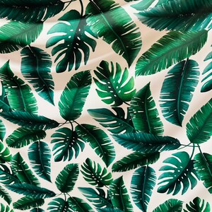 Op de afbeelding: Een witte achtergrond met een herhalend patroon van groene tropische bladeren. De bladeren zijn in verschillende vormen en maten, waaronder palmbladeren en monstera bladeren.