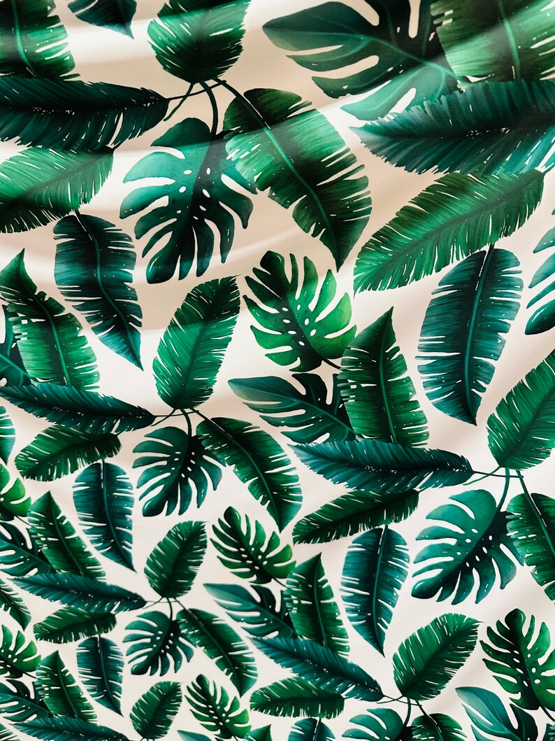 Op de afbeelding: Een witte achtergrond met een herhalend patroon van groene tropische bladeren. De bladeren zijn in verschillende vormen en maten, waaronder palmbladeren en monstera bladeren.