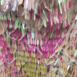 Può includere: Primo piano di paillettes iridescenti in tonalità bianche, rosa e gialle. Le paillettes sono disposte a formare un motivo e cucite su un tessuto a rete.