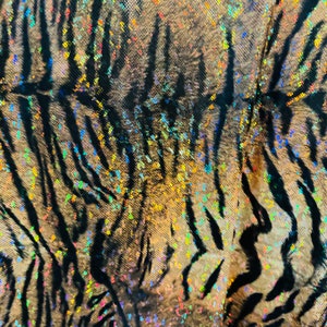 May include: Close-up of a fabric with a tiger stripe pattern. The fabric is iridescent and has a glittery finish. The stripes are black and the background is a light brown color.