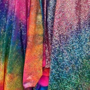 K&ouml;nnte beinhalten: Nahaufnahme von irisierendem Stoff in den Farben Pink, Blau, Gr&uuml;n und Orange. Der Stoff hat eine strukturierte, glitzernde Oberfl&auml;che.