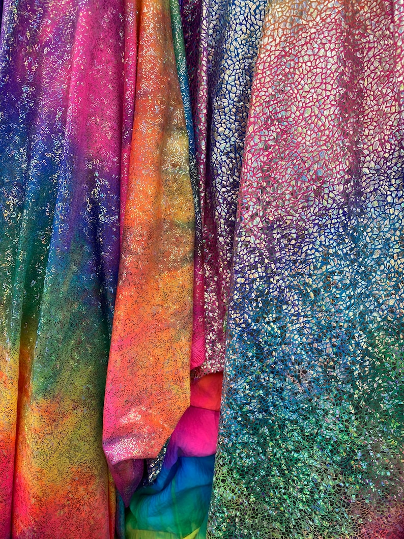 K&ouml;nnte beinhalten: Nahaufnahme von irisierendem Stoff in den Farben Pink, Blau, Gr&uuml;n und Orange. Der Stoff hat eine strukturierte, glitzernde Oberfl&auml;che.
