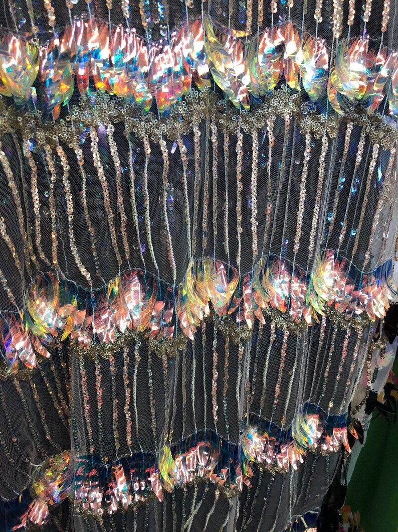 K&ouml;nnte beinhalten: Nahaufnahme eines irisierenden Stoffes mit Pailletten und Perlen. Der Stoff hat eine schwarze Netzbasis mit Reihen von irisierenden Pailletten und Perlen. Die Pailletten sind in einem Muster &uuml;berlappender Bl&auml;tter angeordnet.