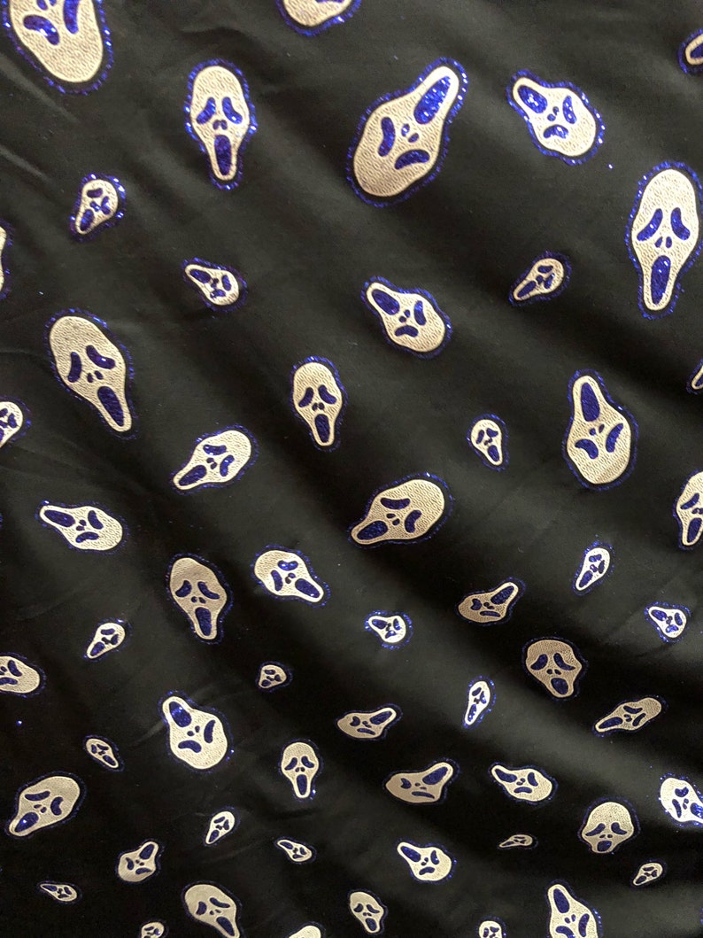 May include: Black fabric with a repeating pattern of white ghost face masks with blue glitter accents.