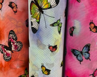 May include: Three rolls of fabric with a butterfly print. The fabric is sheer and has a watercolor effect. The butterflies are in shades of pink, blue, green, and yellow.
