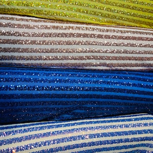 May include: Close-up of several rolls of fabric with horizontal stripes of sequins. The fabrics are in various colors, including yellow, brown, blue, and white with blue stripes. The sequins add a shimmering effect to the textiles.