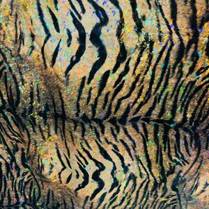May include: A close-up of a fabric with a tiger stripe pattern. The fabric is a light brown color with black stripes and iridescent glitter accents.