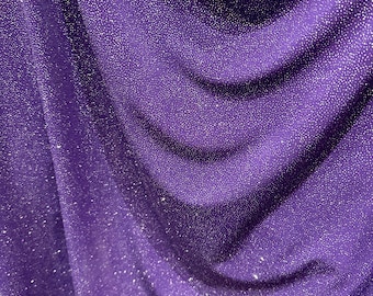 May include: Purple fabric with a sparkly, glittery texture. The fabric is draped and folded, creating a soft, flowing look.