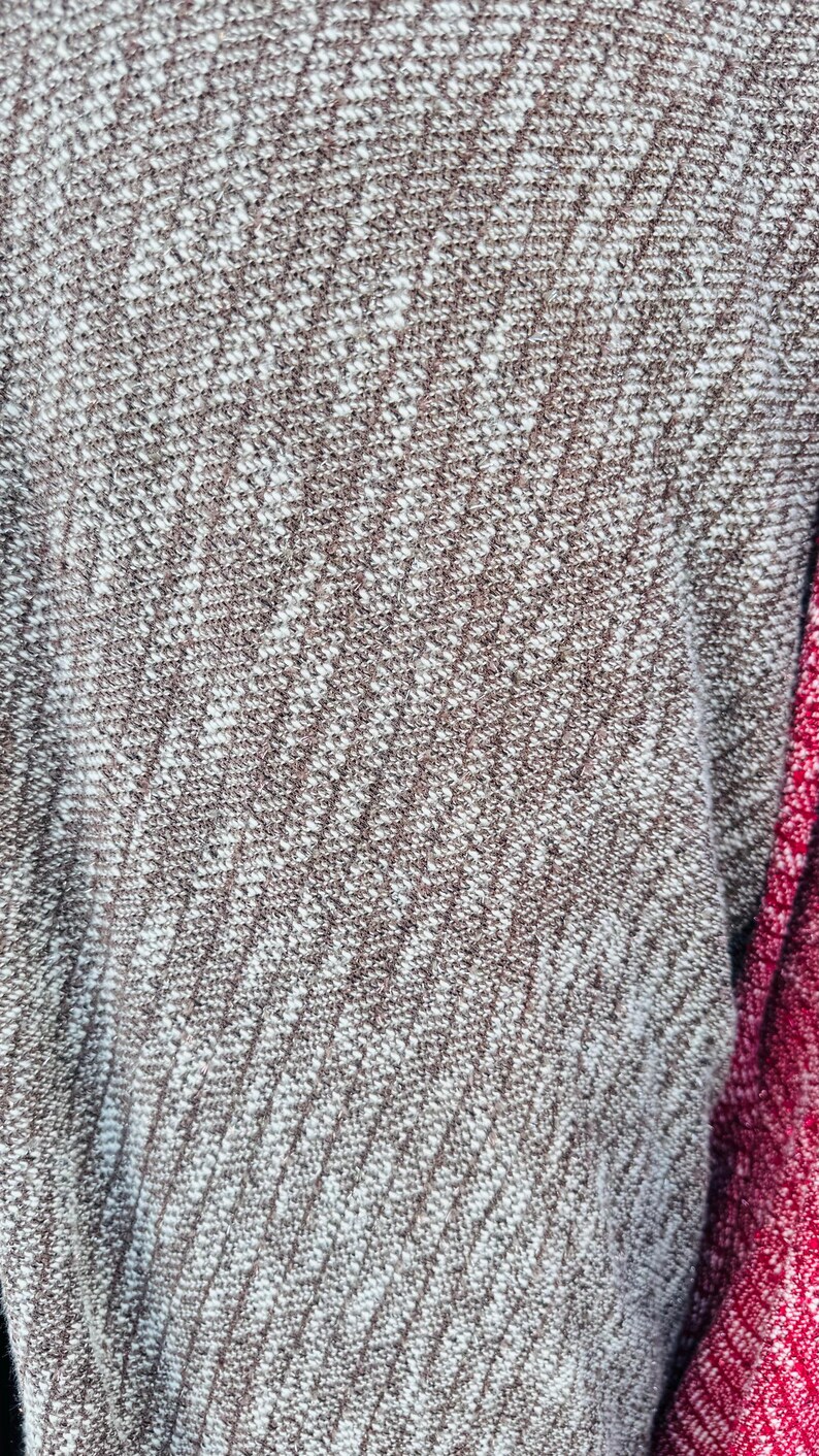 K&ouml;nnte beinhalten: Nahaufnahme eines braunen und wei&szlig;en Strickstoffes mit diagonalem Muster. Der Stoff ist weich und texturiert, mit einem dezenten Glanz.