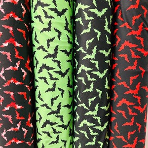 Op de afbeelding: Vier rollen stof met een zwart vleermuispatroon. De stof is verkrijgbaar in rood, groen en zwart.