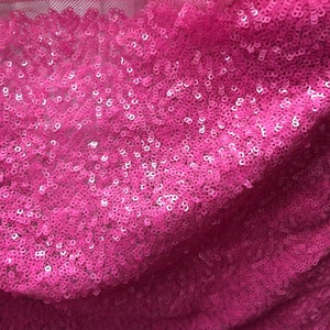May include: Pink sequined fabric with a mesh backing. The sequins are small and closely packed together, creating a shimmering effect.