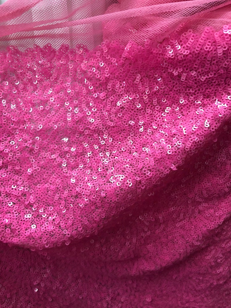 May include: Pink sequined fabric with a mesh backing. The sequins are small and closely packed together, creating a shimmering effect.